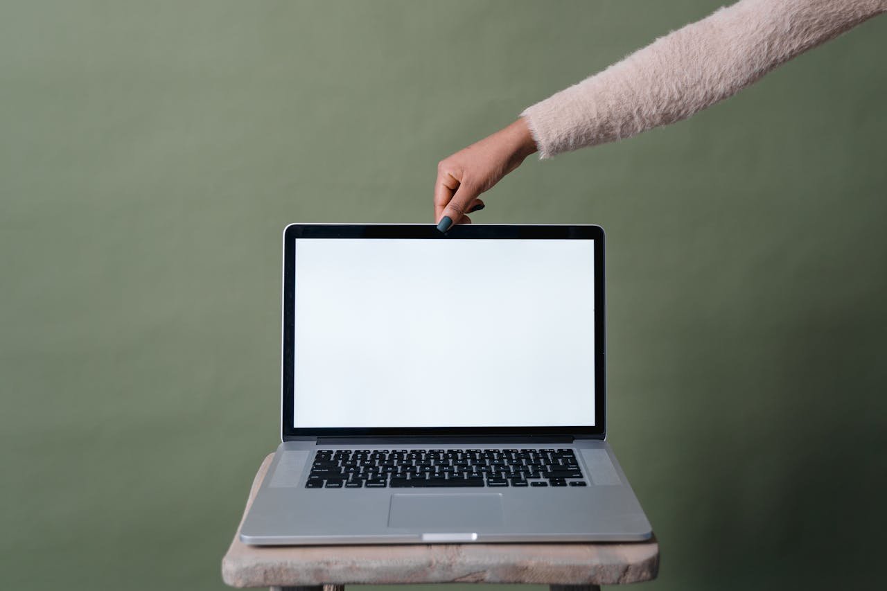 A hand holding open a laptop with a blank screen against a green background, ideal for mockup use.